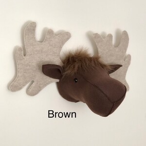 May include: Brown felt moose head wall decor with large, beige felt antlers. The moose head has a furry brown face and black eyes.