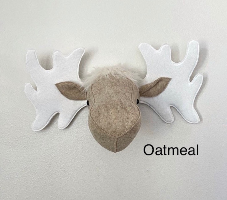 May include: A beige felt moose head with white felt antlers. The moose head is a wall decoration and has the word "Oatmeal" written below it.