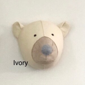May include: A plush ivory polar bear head with a brown nose and blue snout. The bear head is a wall decoration.