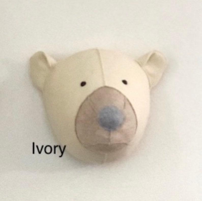 May include: A plush ivory polar bear head with a brown nose and blue snout. The bear head is a wall decoration.