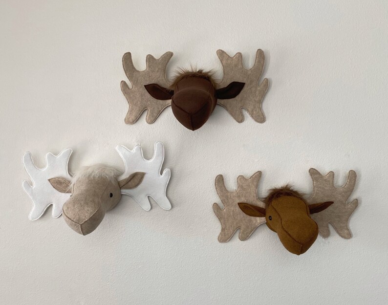 May include: Three felt moose head wall decorations. One is brown with beige antlers, one is beige with white antlers, and one is brown with beige antlers.