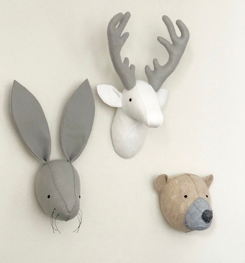May include: Three felt animal head wall decorations. A white deer head with gray antlers, a gray rabbit head with long ears, and a brown bear head with gray fur.