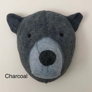 May include: A charcoal gray felt bear head wall decor with black eyes and a gray felt nose.