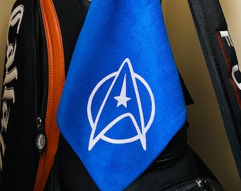 May include: A blue golf towel with a white Star Trek logo. The towel is hanging on a black golf bag.