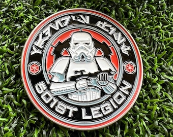 May include: A round, silver-colored metal pin with a black and red design. The pin features a white Stormtrooper from Star Wars with the text "501st Legion" and "YEVMAW EKVW" in black and white.