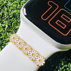 May include: White Apple Watch band with a gold daisy chain design. The band is shown on a green background.