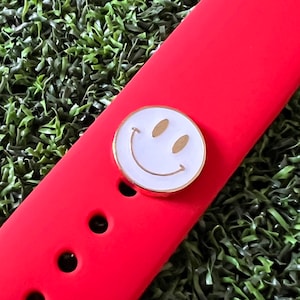 K&ouml;nnte beinhalten: Ein rotes Silikon-Armband mit einem goldenen, wei&szlig;en Smiley-Anh&auml;nger.
