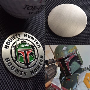 Puede incluir: Una moneda de metal plateado con las palabras "BOUNTY HUNTER" alrededor del borde. El centro de la moneda presenta un casco Boba Fett verde y rojo.