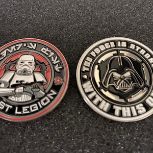 May include: Two collectible coins featuring Star Wars characters. One coin depicts a Stormtrooper with "501st Legion" text. The other coin shows Darth Vader with the text "The Force is Strong With This One!"