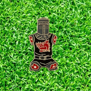 May include: Black enamel pin of a knight in armor with a red boar head on the chest. The knight is wearing a helmet with a visor and has a red and black design on the armor.