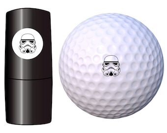 May include: A white golf ball with a black and white image of a Star Wars Stormtrooper helmet on it. The golf ball is next to a black tube with a white circle containing the same image.