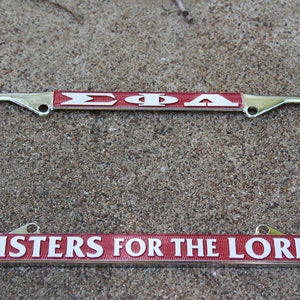 May include: A silver licence plate frame with a red and white band that says "ΣΦΑ SISTERS FOR THE LORD".
