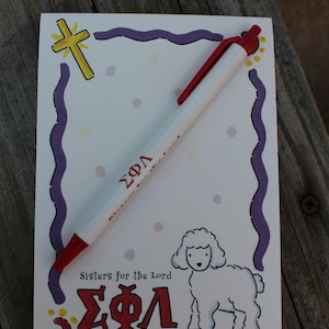 May include: A white notepad with a purple and blue border, a red pen, and a white lamb illustration. The notepad has the text "Sisters for the Lord" and "ΣΦΛ" in red. The notepad also has a yellow cross with a gold outline.