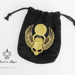 May include: Black velvet drawstring bag with a gold embroidered scarab beetle design. The bag features a gold sun disc above the beetle and wings. The bag is labeled "Back to Magic".