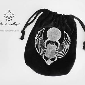 May include: Black velvet drawstring bag with a detailed silver embroidered scarab beetle design. The bag features the text "Back to Magic" and is photographed by Anat Or Lev.