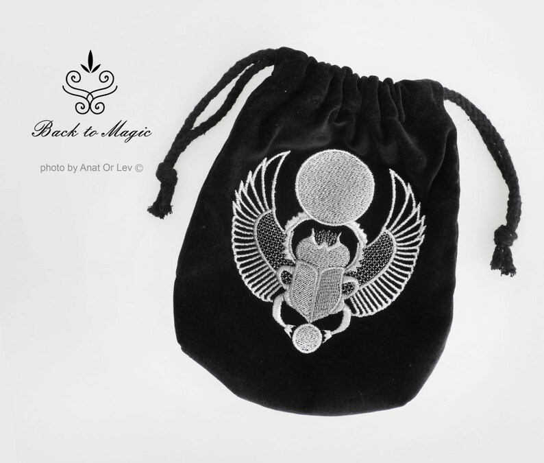 May include: Black velvet drawstring bag with a detailed silver embroidered scarab beetle design. The bag features the text "Back to Magic" and is photographed by Anat Or Lev.