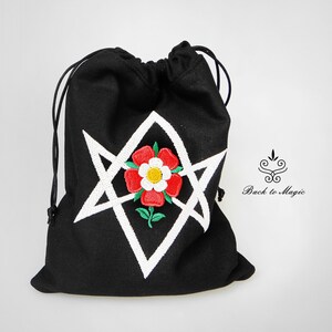 Op de afbeelding: Zwarte trekkoordtas met een wit pentagram en een rode roos geborduurd op de voorkant. De tas heeft een wit trekkoord en de tekst "Back to Magic" is zichtbaar op de achtergrond.
