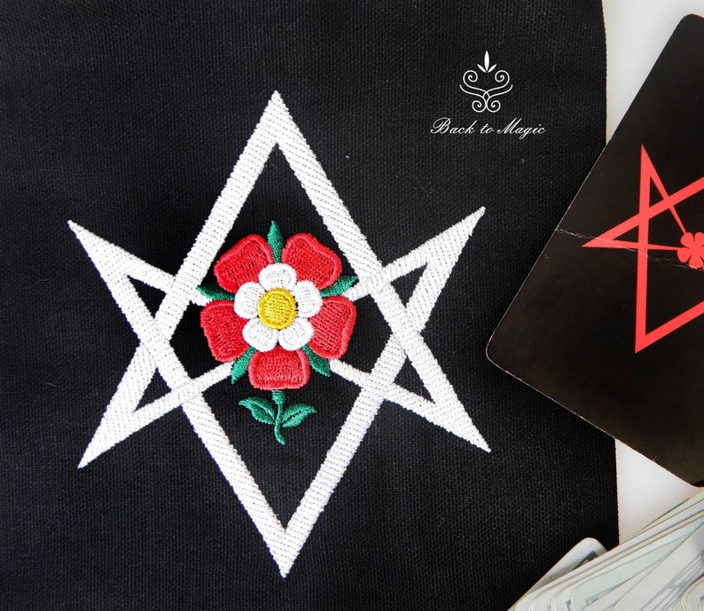 Op de afbeelding: Witte geborduurde pentagram met een rode roos in het midden op een zwarte stoffen achtergrond. De tekst "Back to Magic" is zichtbaar in de rechterbovenhoek.