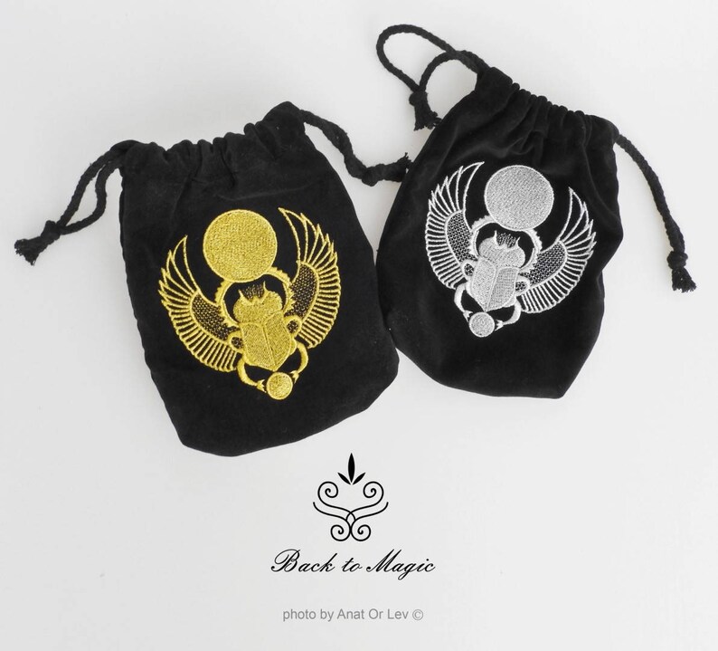 May include: Two black velvet drawstring bags with embroidered scarab beetle designs. One bag features a gold beetle, the other a silver beetle. The bags have black drawstrings. The text "Back to Magic" is below the bags.