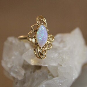 May include: A delicate gold ring with a white opal gemstone set in a filigree design.