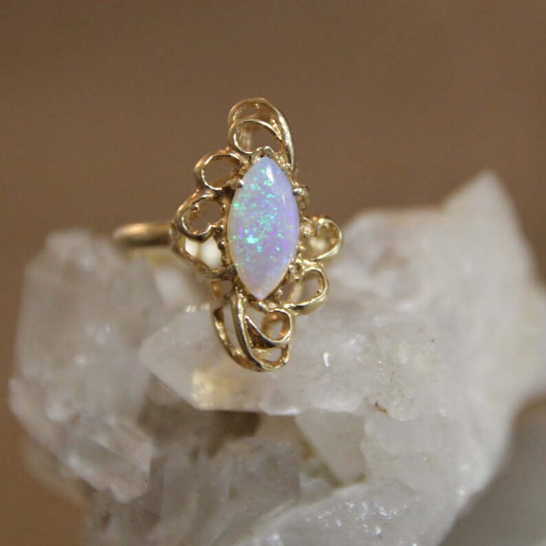 May include: A delicate gold ring with a white opal gemstone set in a filigree design.