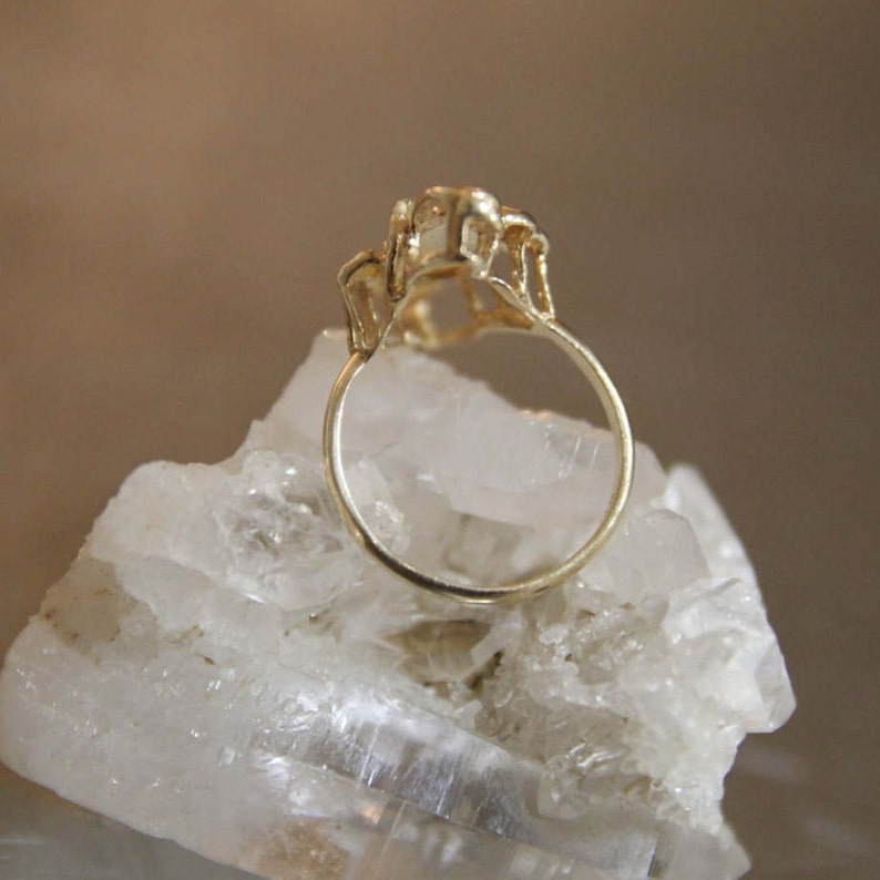 May include: A gold ring with a delicate design featuring three small stones. The ring is sitting on a bed of white crystals.