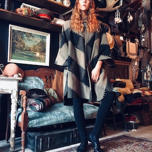 Peut inclure: Une femme portant un poncho à motifs marrons et noirs avec un chapeau noir et un legging noir. Elle se tient dans un magasin avec une variété d'articles sur les étagères derrière elle.