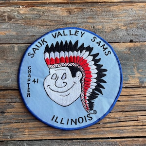May include: A blue and white embroidered patch with the text "SAUK VALLEY SAMS CHAPTER 41 ILLINOIS" and a cartoon image of a Native American wearing a headdress.