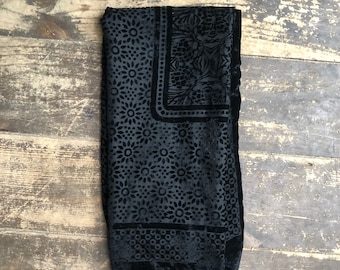 May include: Black velvet scarf with a floral pattern and a border of small circles. The scarf is folded in half and lying on a wooden surface.