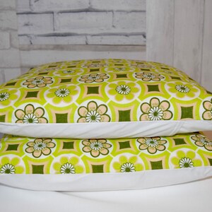 Puede incluir: Dos almohadas de tiro verde y blanco con un dise&ntilde;o geom&eacute;trico. Las almohadas tienen un borde blanco y est&aacute;n apiladas una encima de la otra.