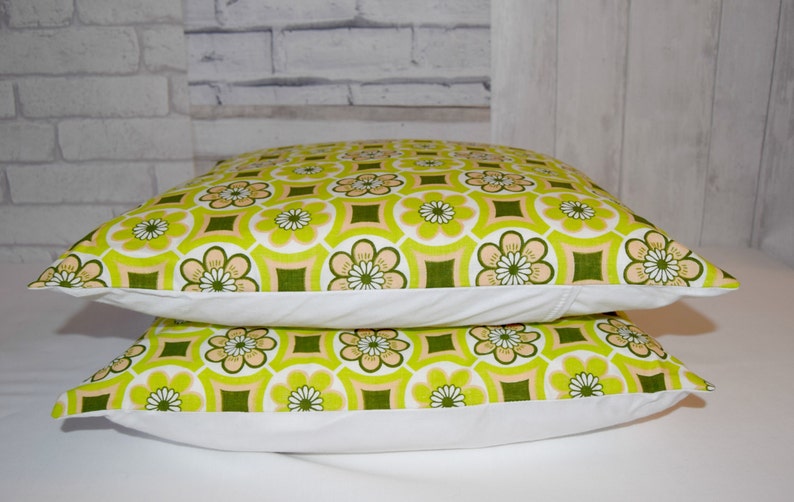 Puede incluir: Dos almohadas de tiro verde y blanco con un dise&ntilde;o geom&eacute;trico. Las almohadas tienen un borde blanco y est&aacute;n apiladas una encima de la otra.