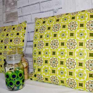 Puede incluir: Dos almohadas de tiro con estampado verde y blanco con un tarro de vidrio decorativo lleno de botones verdes en primer plano.