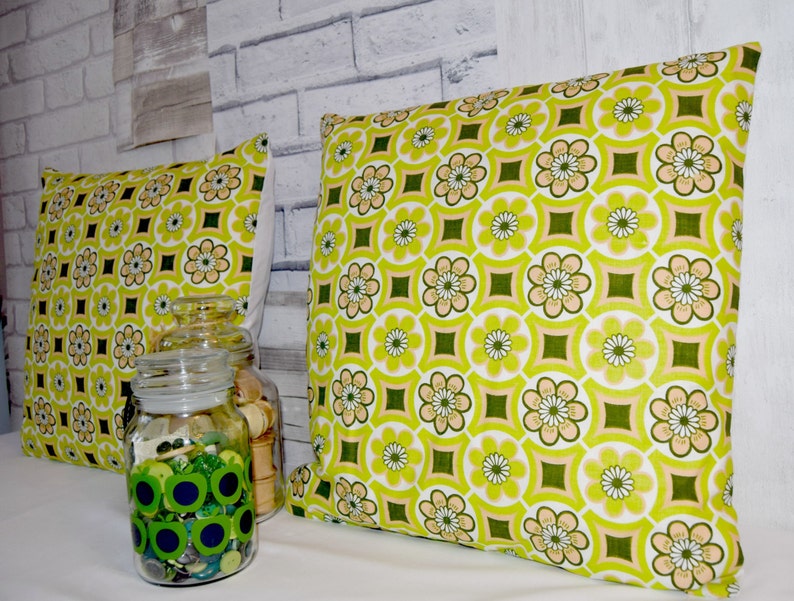 Puede incluir: Dos almohadas de tiro con estampado verde y blanco con un tarro de vidrio decorativo lleno de botones verdes en primer plano.