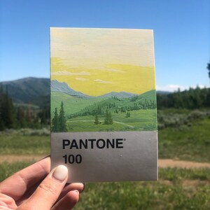 K&ouml;nnte beinhalten: Eine gemalte Landschaftskarte mit gelbem Himmel, gr&uuml;nen H&uuml;geln und ein paar B&auml;umen. Die Karte ist ein Pantone-Farbmuster und die Nummer 100 ist unten aufgedruckt.