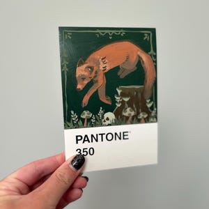 Könnte beinhalten: Rechteckige Karte mit einem Gemälde eines Fuchses, der über einen Baumstumpf springt, mit Pilzen und Totenköpfen. Der Hintergrund ist dunkelgrün. Die Karte trägt unten den Text "PANTONE 350".