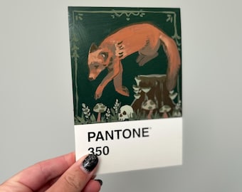 May include: A rectangular card featuring a painting of a fox leaping over a tree stump, with mushrooms and skulls. The background is dark green. The card has the text "PANTONE 350" at the bottom.