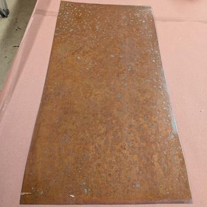 May include: A rectangular metal sheet featuring a heavily oxidized, rusted surface with a mottled texture of deep brown, orange, and small patches of teal patina. The flat, weathered panel displays a consistent, aged appearance across its entire surface.