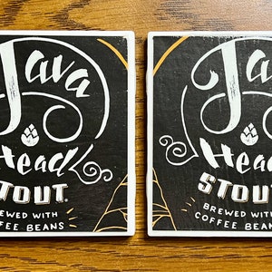 May include: Two black and white coasters with a gold border. The coasters feature a skull with a coffee bean in the center and the text "Java Head Stout. Brewed with Coffee Beans".