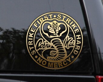 May include: Gold vinyl sticker with a black cobra logo and the text "Strike First Strike Hard No Mercy" around the logo.