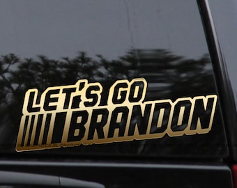 May include: A gold and black vinyl decal with the text "Let's Go Brandon" on a black car window.
