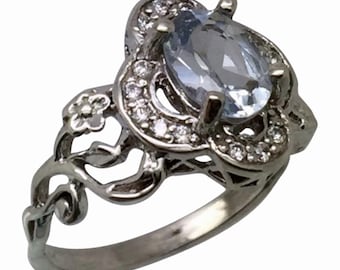 May include: A silver ring with a light blue oval gemstone surrounded by smaller clear gemstones. The ring has a delicate floral design.