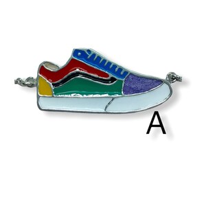 May include: A colorful sneaker charm with a silver chain. The shoe design features sections of red, green, yellow, blue, and purple, outlined in black and white. The letter "A" is visible.