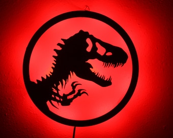 May include: A red light illuminates a black silhouette of a dinosaur inside a circular frame. The dinosaur is a velociraptor, a type of theropod dinosaur.
