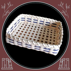 May include: A rectangular woven basket with a white and blue design. The basket is made of woven strips of light-colored material, with blue accents. The basket is designed with a lattice pattern.