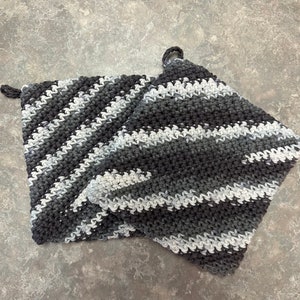 Puede incluir: Dos agarraderas de olla de crochet a rayas grises y blancas. Las agarraderas están hechas con un punto sencillo y tienen un lazo para colgar.