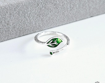 May include: Silver ring featuring a green leaf design. The ring is crafted to resemble a twig with a leaf attached.