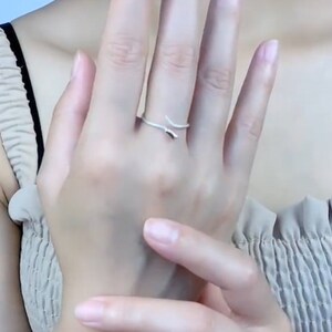 May include: A silver ring with a simple, curved design. The ring is worn on the middle finger of a person's hand.