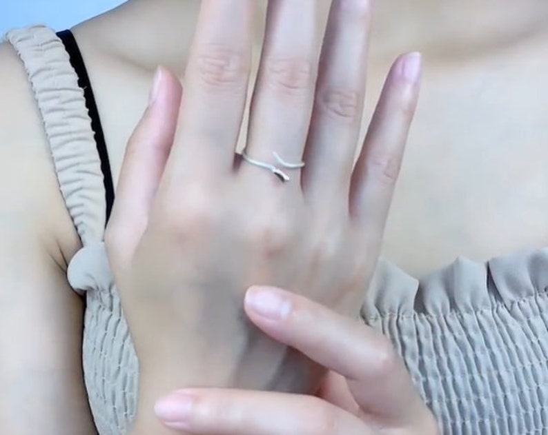 May include: A silver ring with a simple, curved design. The ring is worn on the middle finger of a person's hand.