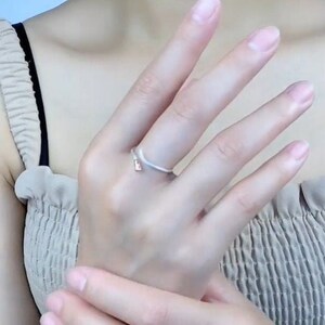 May include: A silver ring with a simple, curved design. The ring is worn on the ring finger of a person's hand.