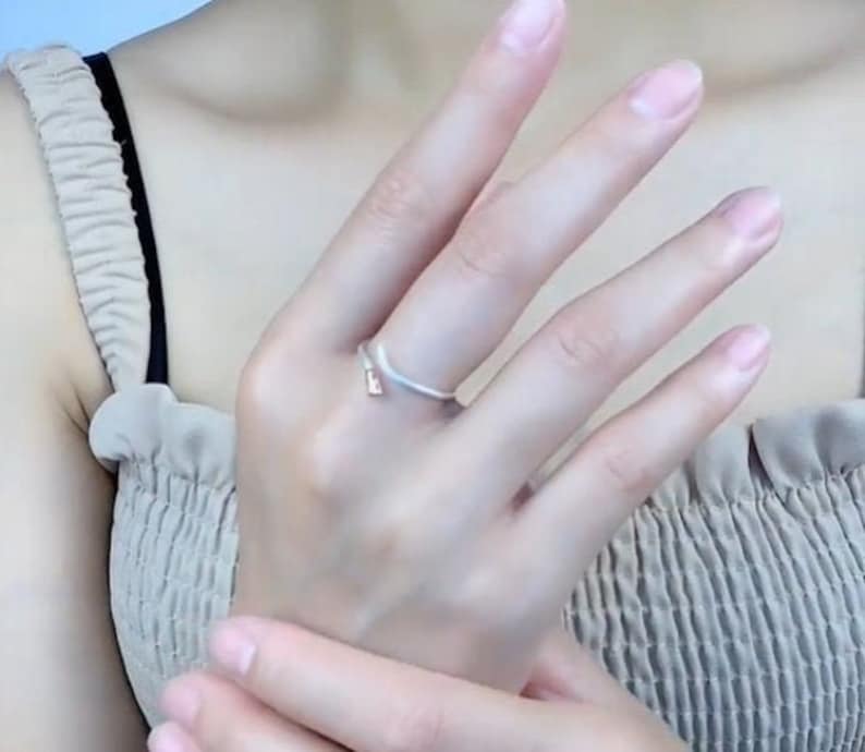 May include: A silver ring with a simple, curved design. The ring is worn on the ring finger of a person's hand.